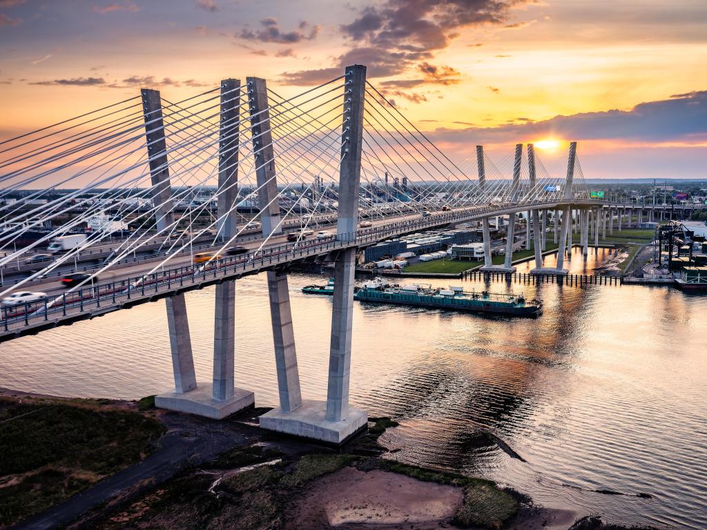 Aerial view of the New Goethals Bridge at sunset, spanning Arthur Kill strait between Elizabeth, New Jersey and Staten Island, New York. A conatiner ship navigates under the bridge.