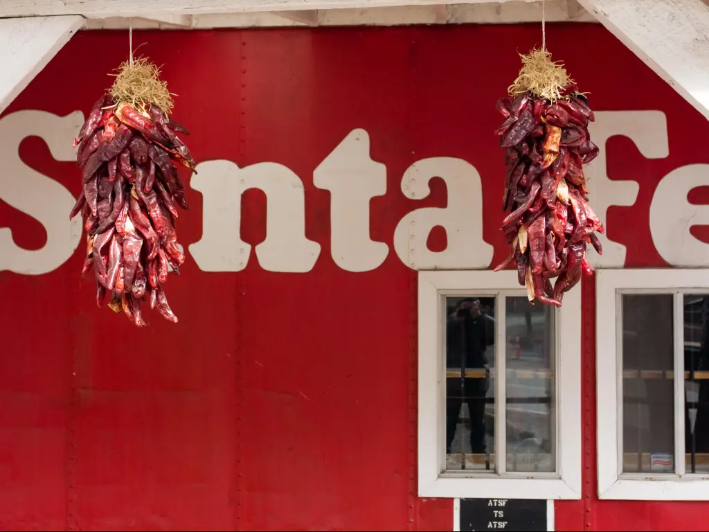 White Santa Fe signage on a red wall, with bunches of red chillies hung drying in front 