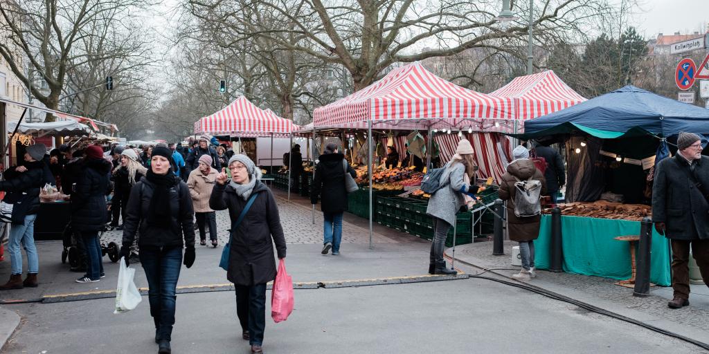 Shoppers carry bags full of produce after visiting the tented stalls at Kollwitzplatz market in Berlin