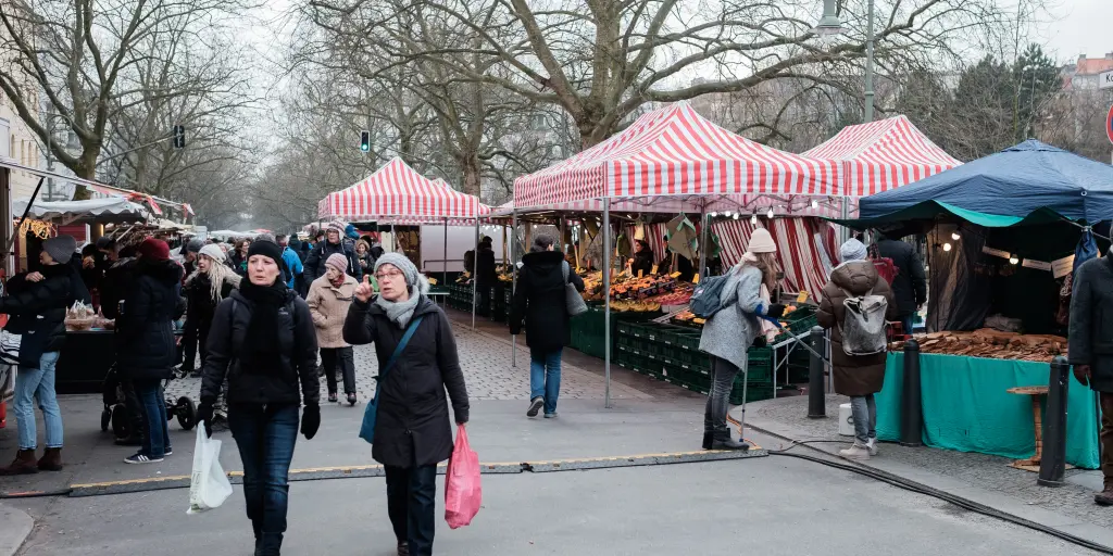 Shoppers carry bags full of produce after visiting the tented stalls at Kollwitzplatz market in Berlin