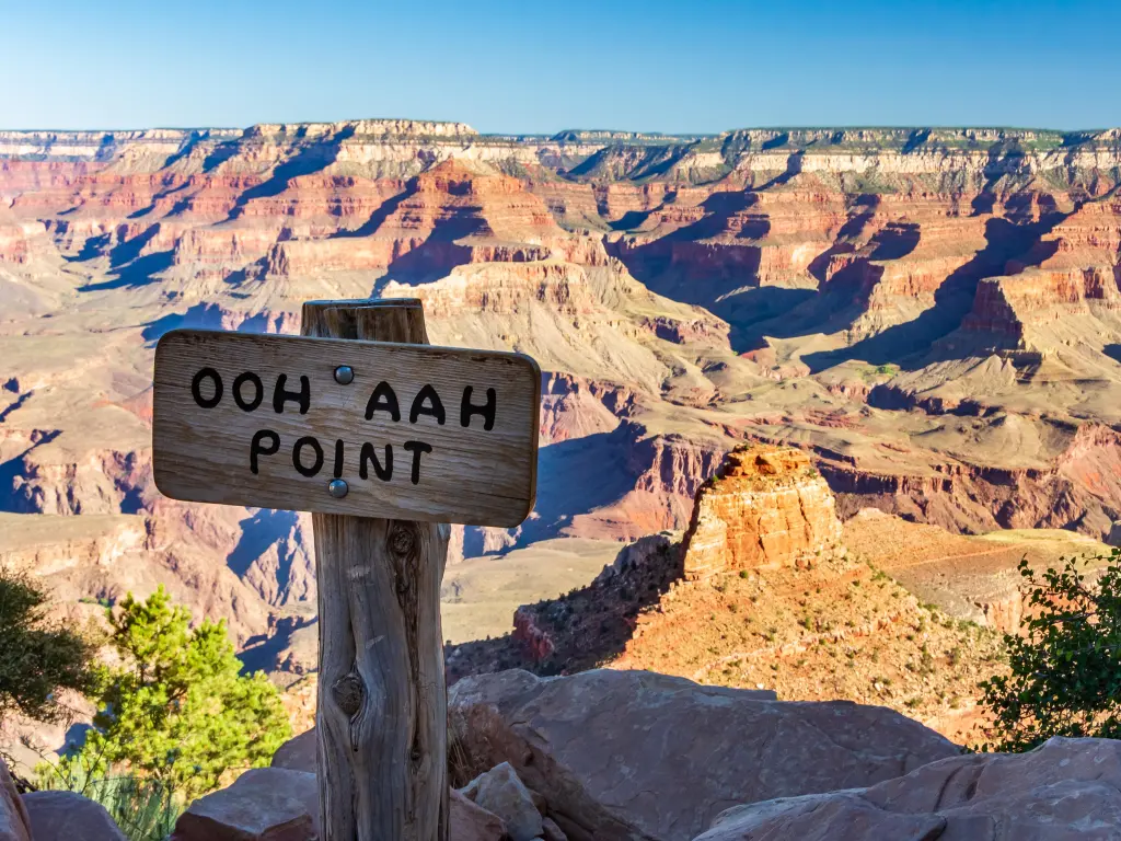 Sign indicating Ooh Aah Point, a panoramic viewpoint in Grand Canyon. Cliffs of sedimentary red rock are visible in the background.