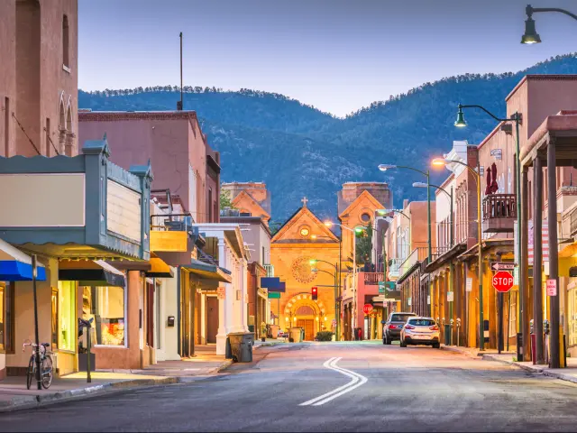 Santa Fe, New Mexico, USA with a scene of the street at early evening and mountains in the distance.