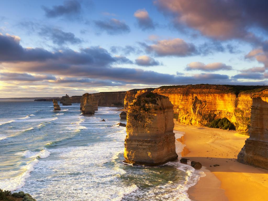 Massive rock formations in a calm ocean with tall cliffs lit up in golden light