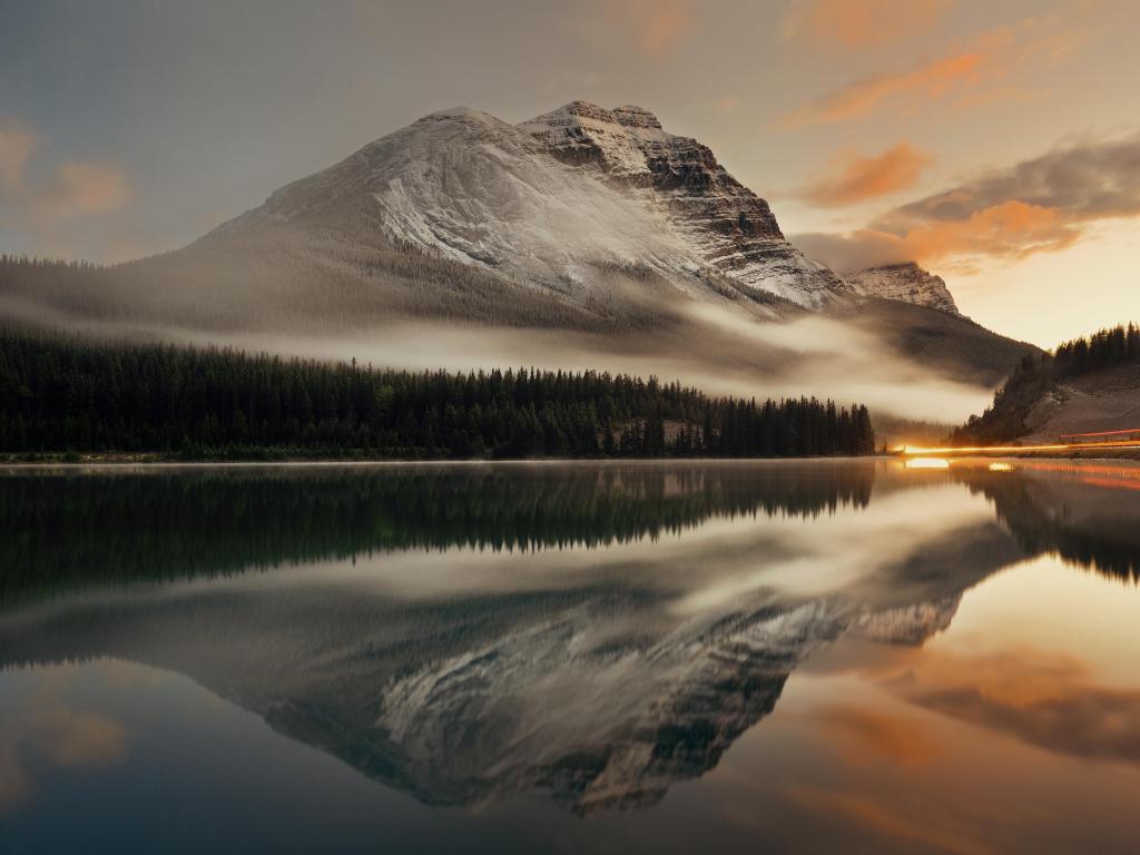 Banff National Park, Canada with the mountain in the distance and lake in the foreground, traffic light trail reflected in the water and fog below the mountains at sunset.
