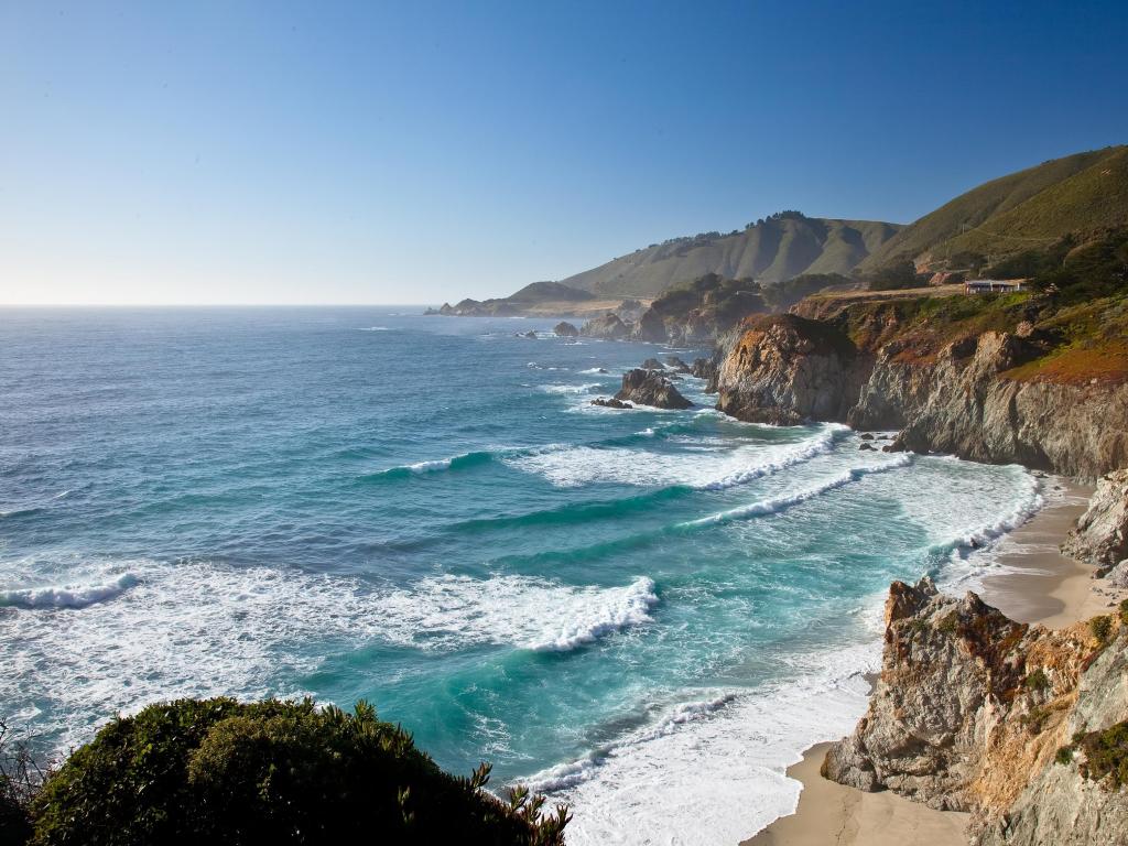 Big Sur, California, USA with rugged cliffs leading to a beach below and turquoise sea taken on a clear sunny day.