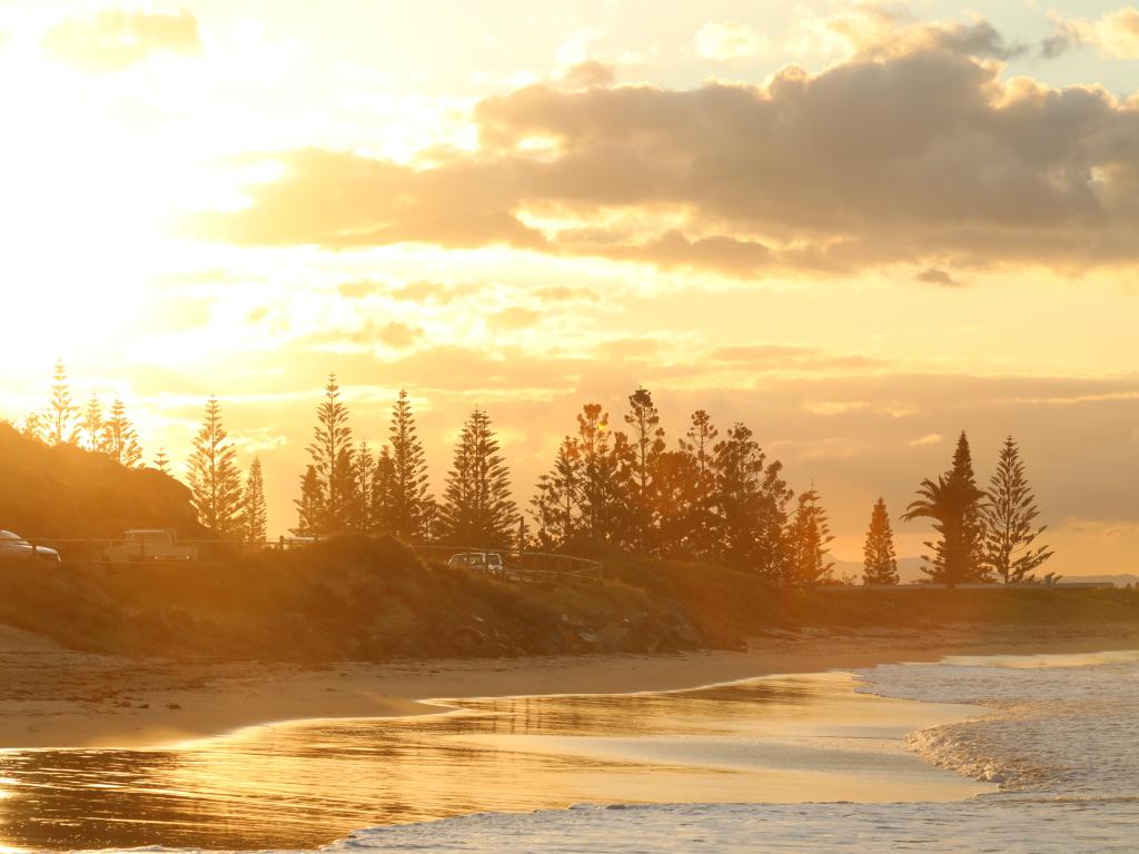 Golden sunset light on empty beach with calm sea breaking on the sand