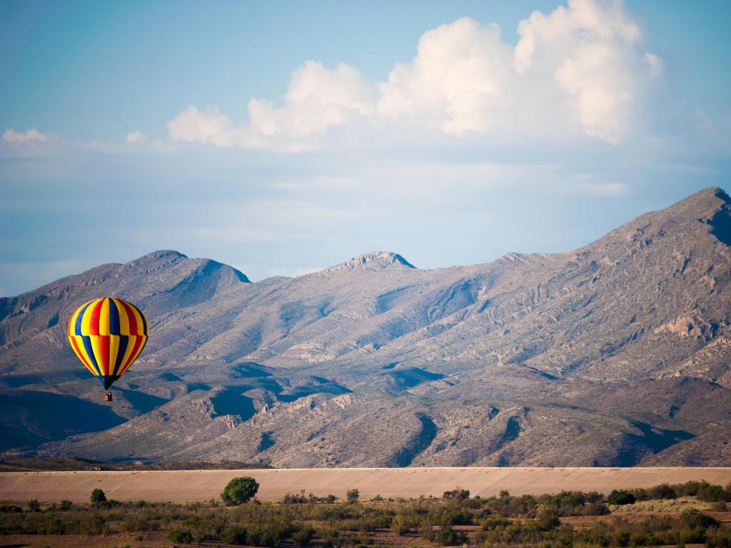 Hot-air balloon in the sky with rugged mountains in the background on a partially cloudy day
