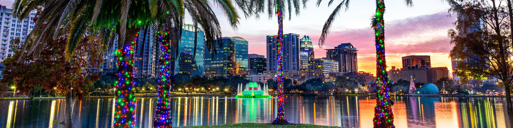 Orlando, Florida, USA downtown skyline at Eola Lake with colorful lights on the palm trees in the foreground.
