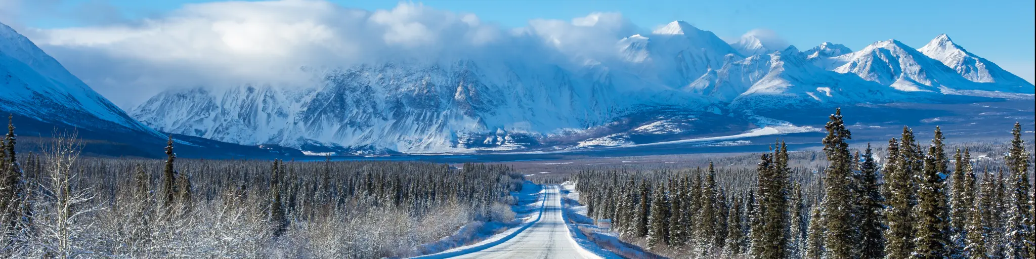 Alaska Highway through the forests of Yukon heading towards mountains in the winter