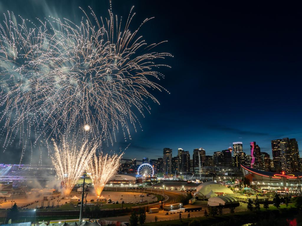 Large fireworks above showground at night, with city skyline illuminated to the right