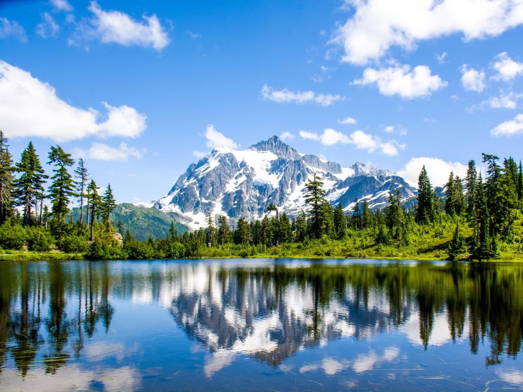 North Cascades National Park, Washington, USA with the landscape of Mount Shuksan reflecting in Picture lake in the foreground and surrounded by trees on a sunny day. 