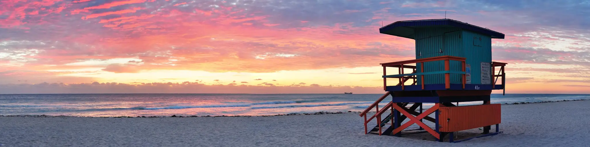 A panoramic view of Miami's South Beach at sunset, with a turqoise-painted lifeguard tower standing on the sand