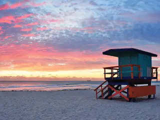 A panoramic view of Miami's South Beach at sunset, with a turqoise-painted lifeguard tower standing on the sand