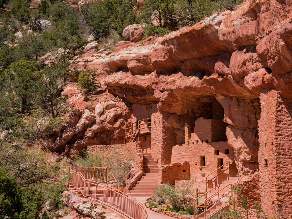 Manitou Cliff Dwellings museum at Manitou Springs, Colorado with steps and windows carved into the orange rocks and trees growing on the mountain side.