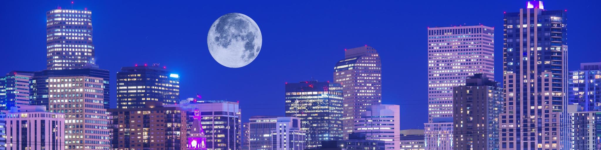 Denver skyline with lights on in the buildings and a big full moon in the sky