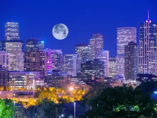 Denver skyline with lights on in the buildings and a big full moon in the sky