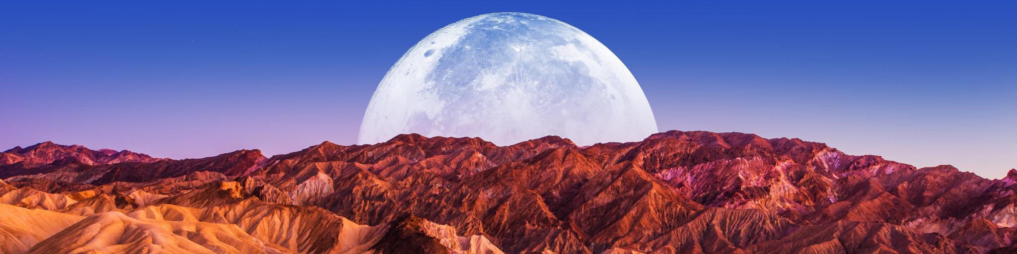 The moon rising over the rugged red rocks of Death Valley National Park