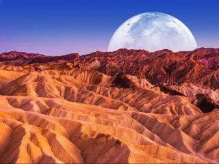The moon rising over the rugged red rocks of Death Valley National Park
