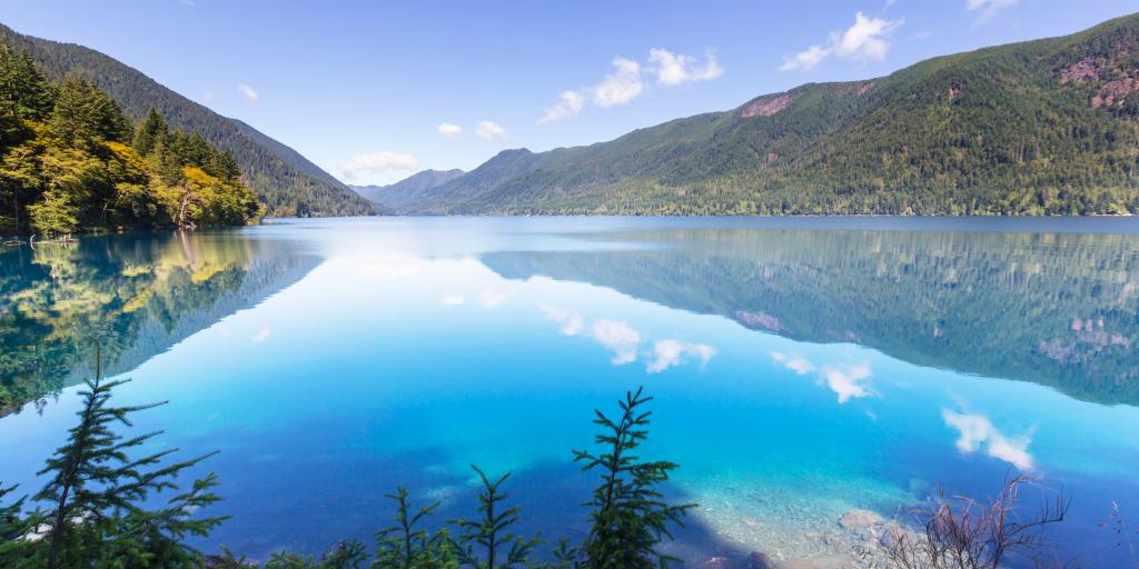 Mountains, blue sky and clouds reflect on the clear surface of Crescent Lake in Washington's Olympic National Park