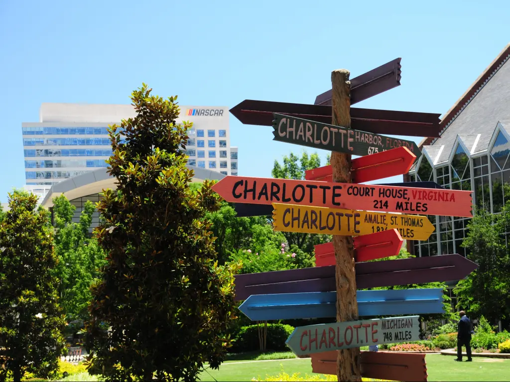 A "Charlotte" directional sign sculpture on "The Green" in Uptown Charlotte seemingly points the the sign of the NASCAR Hall of Fame in the distance.