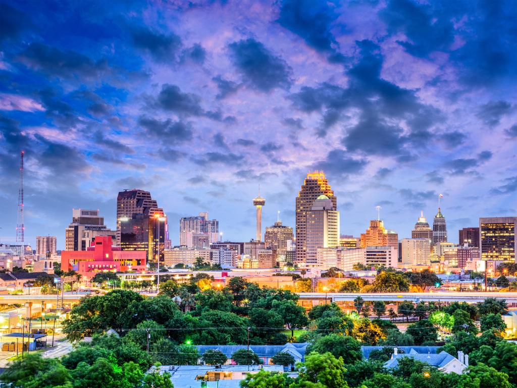 San Antonio, Texas, USA downtown with the city skyline in the distance and green trees in the foreground at sunset with a dramatic sky.