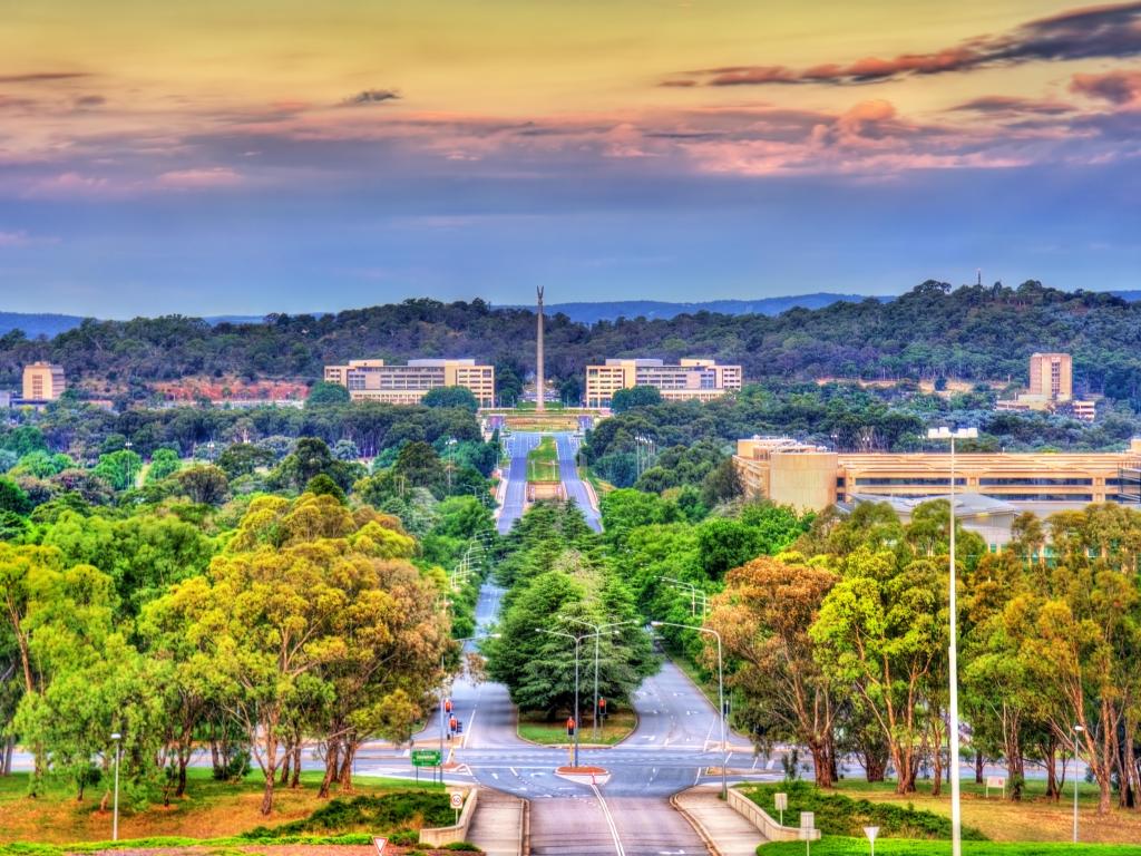 Canberra, Australia with trees lining the road leading to towards the memorial in the distance at sunset. 