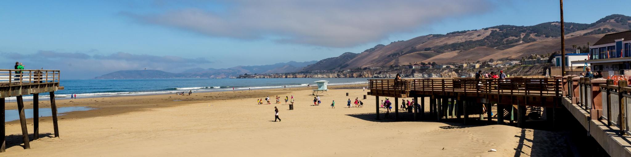 View across sandy beach and boardwalk at Pismo Beach, with bright blue skies and ocean in the background