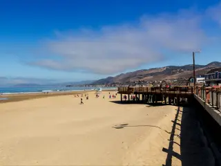 View across sandy beach and boardwalk at Pismo Beach, with bright blue skies and ocean in the background