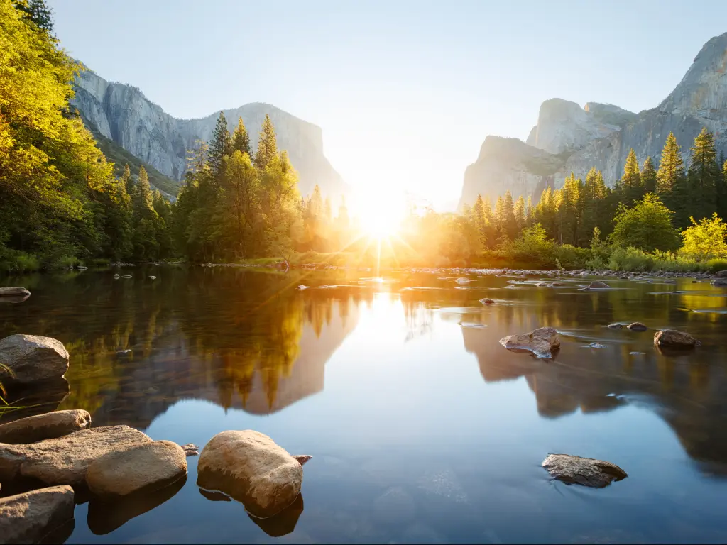 Sunrise through Yosemite Valley with the Merced River in the foreground.