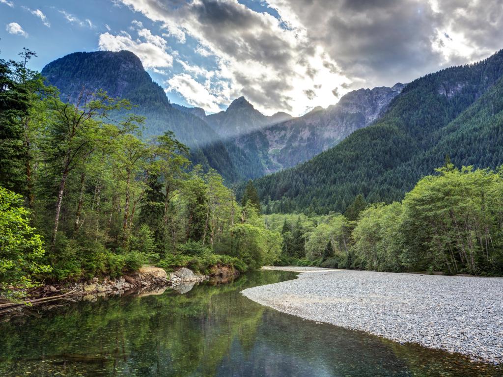 Golden Ears Provincial Park, Canada with a river and forest one side and tree-lined mountains in the distance on a sunny day.