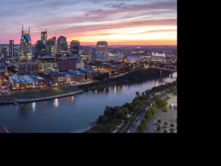 Two bridges cross the river runs that through the city with high rise buildings illuminated on the riverbank.