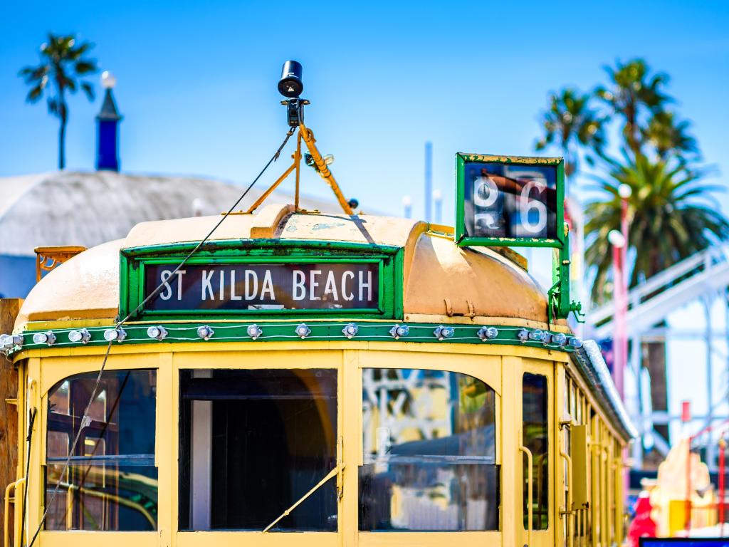 Vintage yellow tram with blurred background of palm trees and fair ground rides in front of a blue sky
