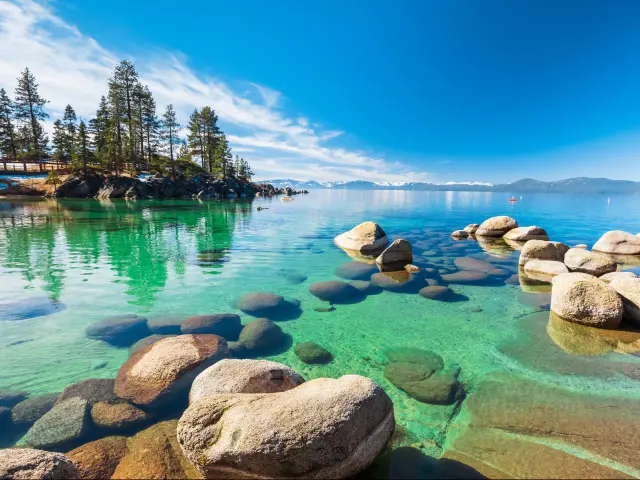 Lake Tahoe rocky shoreline in sunny day, beach with blue sky over clear transparent water