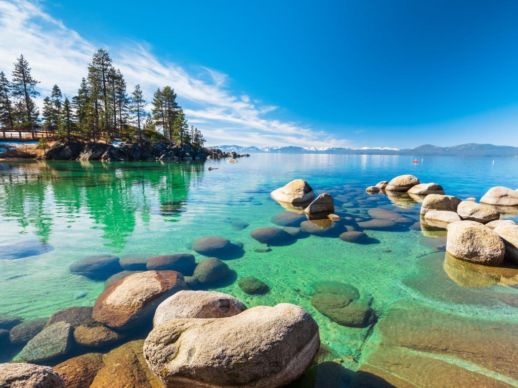 Lake Tahoe rocky shoreline in sunny day, beach with blue sky over clear transparent water