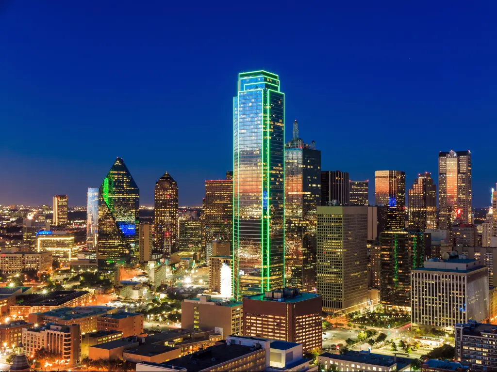 Dallas, Texas, USA with the cityscape at night against a blue sky.