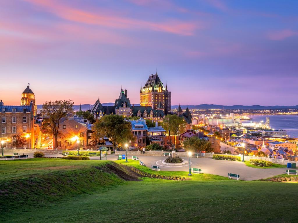 Quebec City, Canada taken as a panoramic view of the city skyline with Saint Lawrence river in the background and taken at early evening with a large grass area in the foreground. 