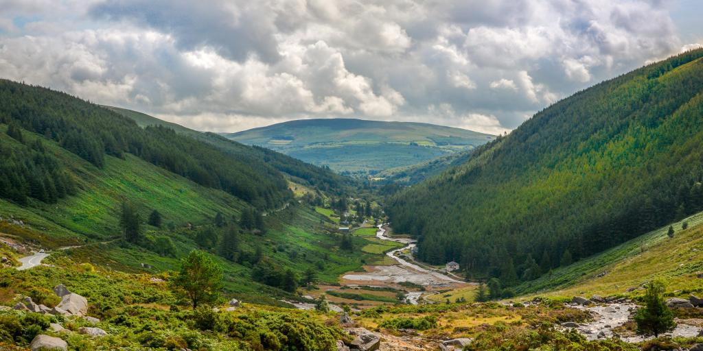 A river cuts through the lush green Glendalough Valley in County Wicklow, Ireland