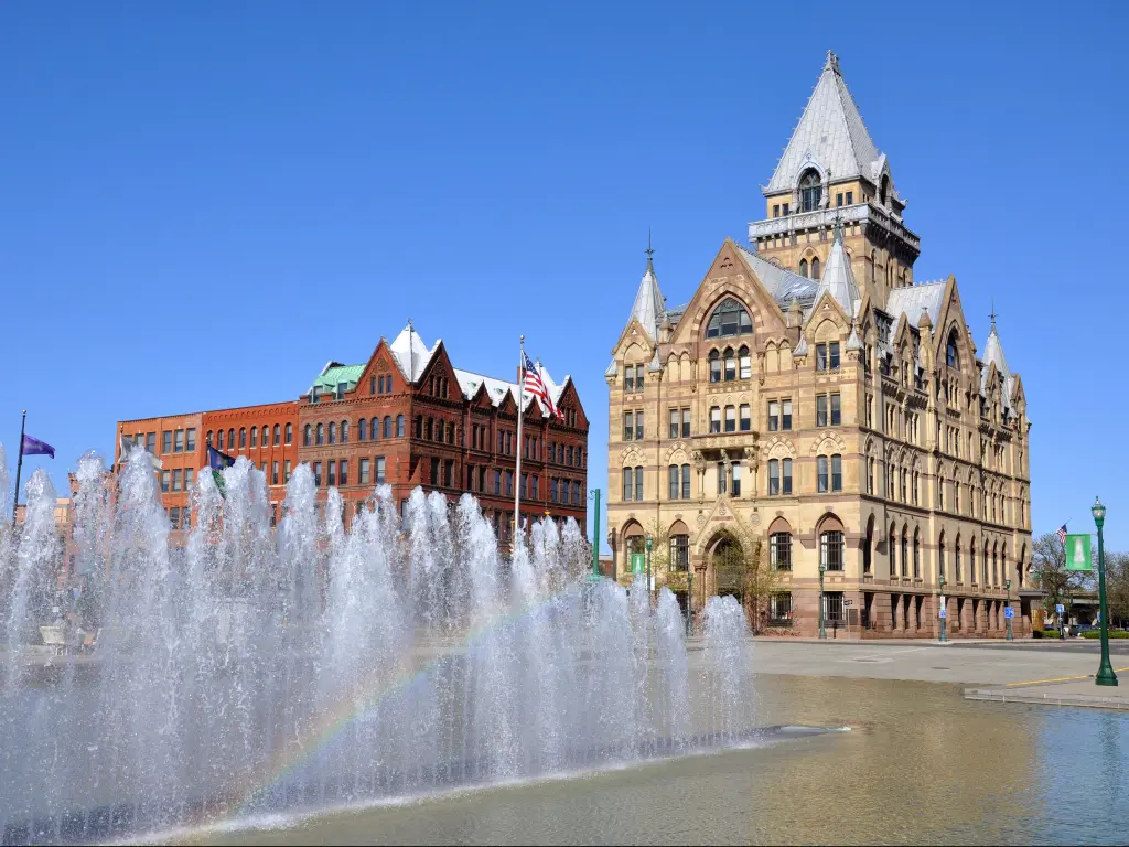 Fountain with rainbow in a square in front of ornate building