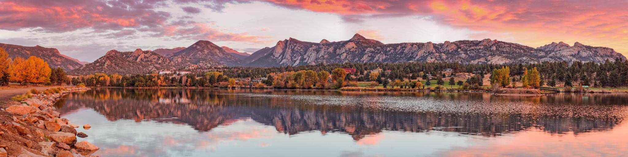 Rocky Mountain National Park, Colorado with a fiery Sunrise over Estes Park, with a lake in the foreground and trees in autumn colour and mountains in the background on the horizon. 