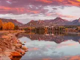 Rocky Mountain National Park, Colorado with a fiery Sunrise over Estes Park, with a lake in the foreground and trees in autumn colour and mountains in the background on the horizon. 