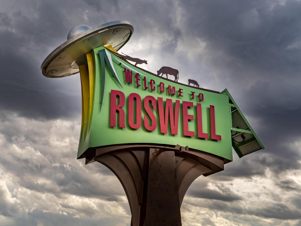 Welcome to Roswell (New Mexico) sign with animals beaming into a flying saucer spaceship.