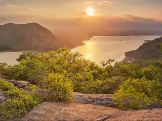 View over wide Hudson River with green trees covering the steep river sides and a bright setting sun