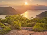 View over wide Hudson River with green trees covering the steep river sides and a bright setting sun