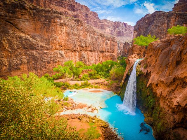 Grand Canyon, Arizona, USA taken at the Havasupai Indian Reservation with an amazing waterfall surrounded by cliffs and trees taken on a sunny day.