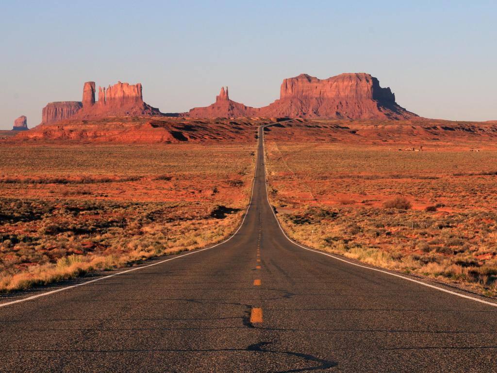 The road to Monument Valley stretching out towards the horizon, with the distinctive red rocks towering over either side