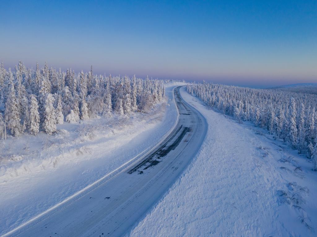 The Dalton Highway ice road in the middle of the winter passing through a conifer forest in northern Alaska.