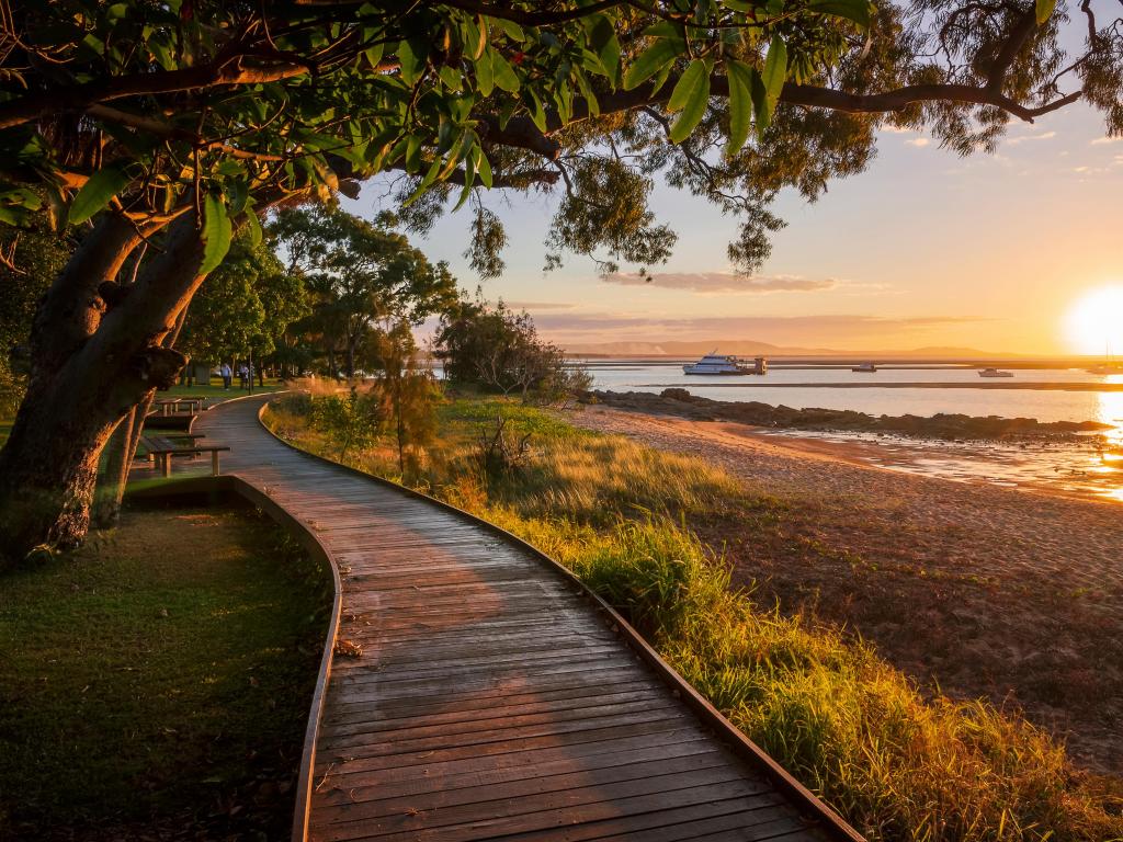 Boardwalk next to sandy beach with vibrant sun set over the ocean and small boats