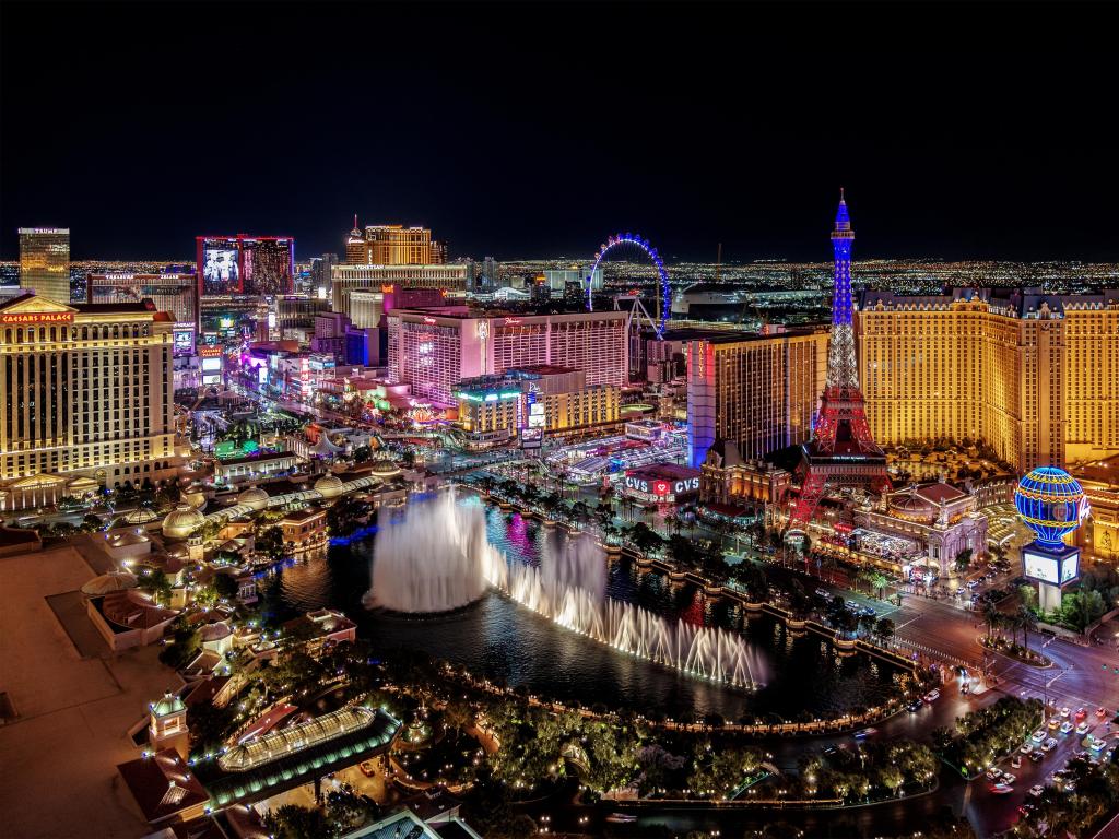A panoramic view of Las Vegas at night showing water fountains and city buildings in the background.