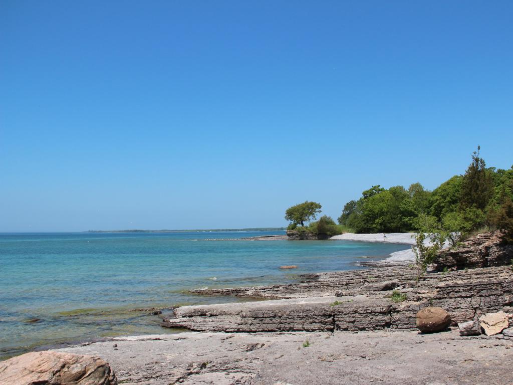 Prince Edward County, Ontario, Canada with the coastline of Lake Ontario in the foreground and rocky beach leading to a calm sea on a sunny clear day. 