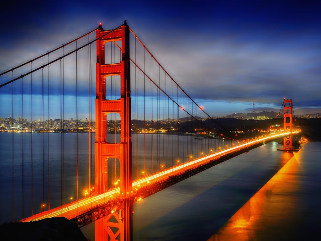 Golden Gate Bridge, San Francisco at night, with San Francisco in the distance and the bridge lit up in yellows, reds and oranges.